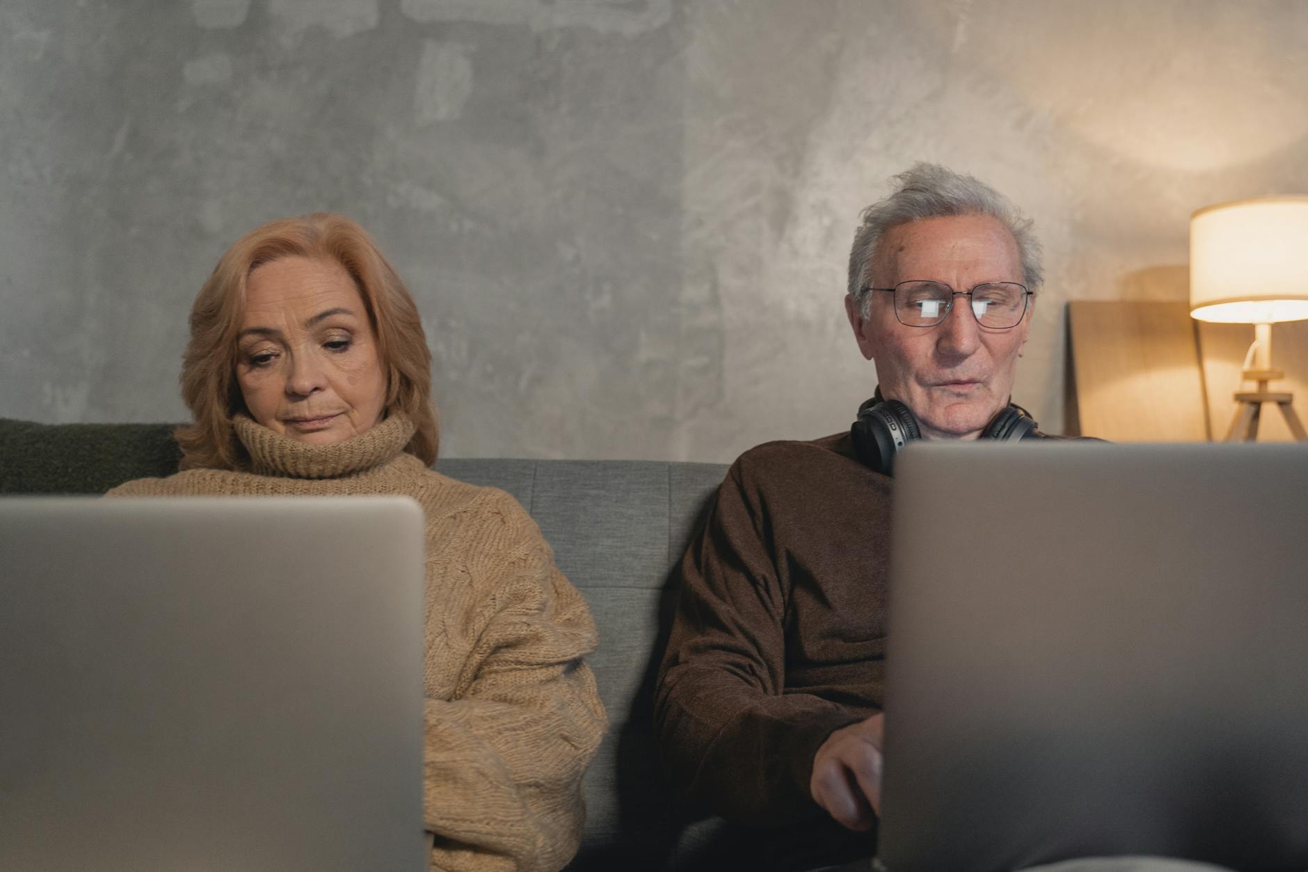 elderly man and woman sitting on couch using laptop computers