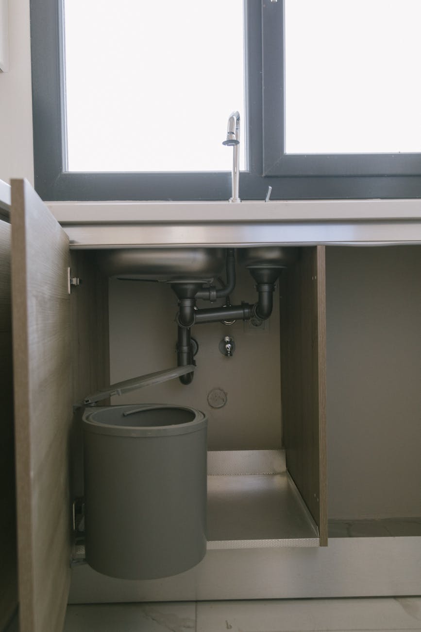 gray garbage can under kitchen sink