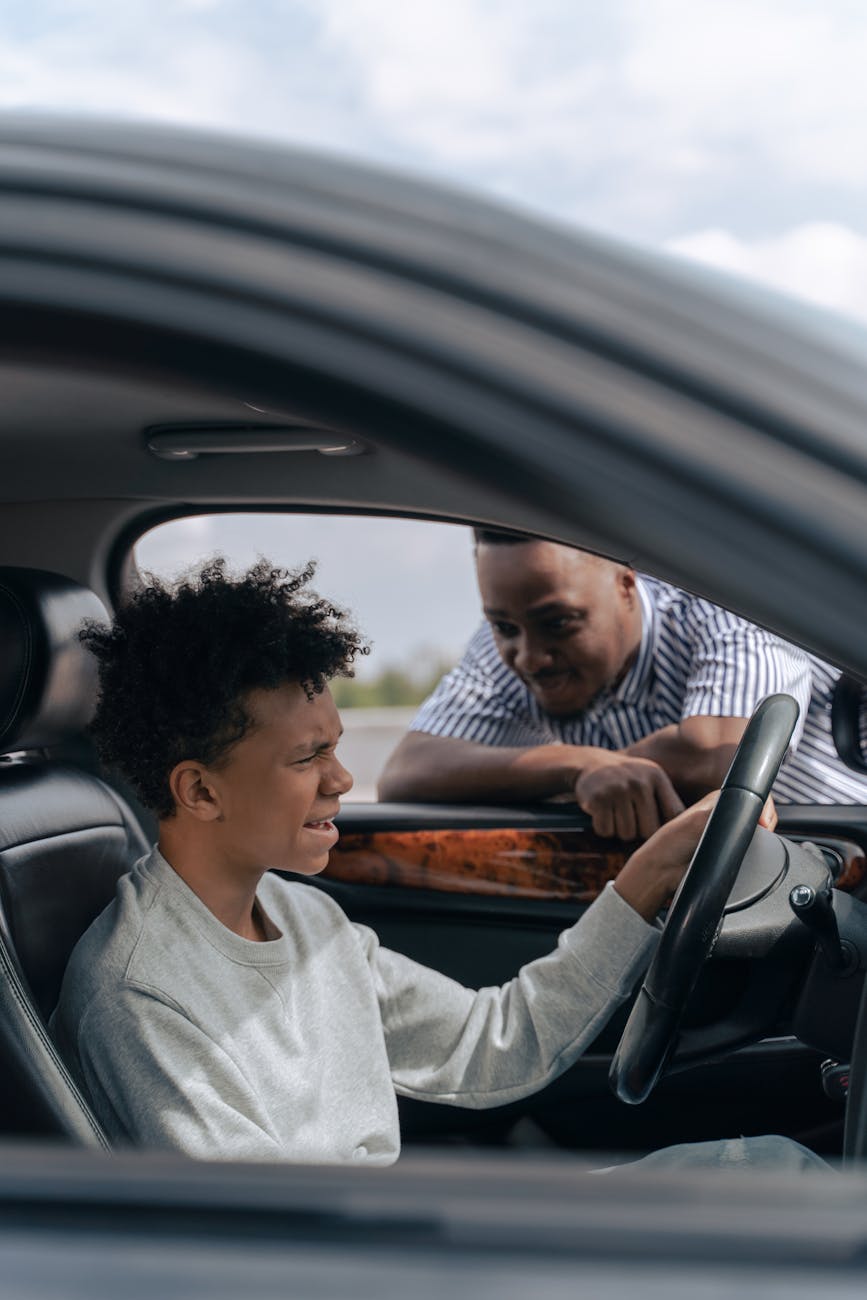 adult man looking at a teenager seated on driver s side of a car