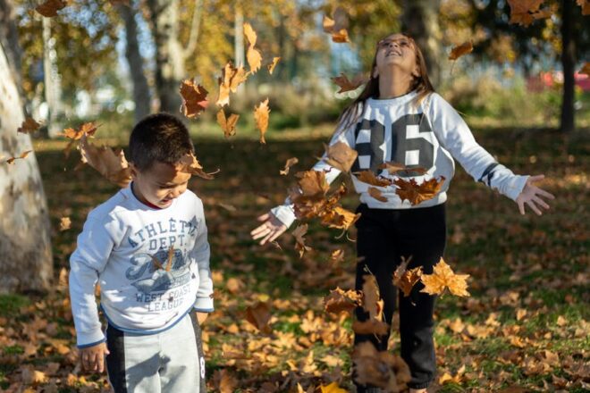 children playing with autumn leaves in park