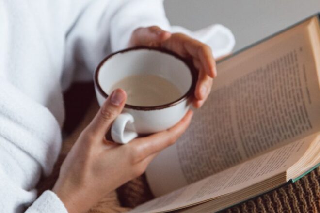 a person holding a ceramic cup while reading a book