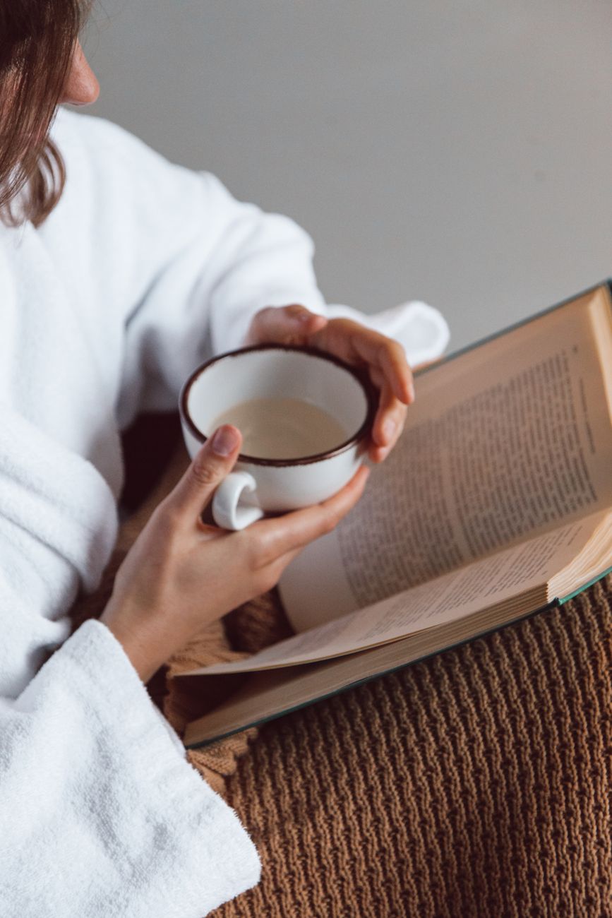 a person holding a ceramic cup while reading a book