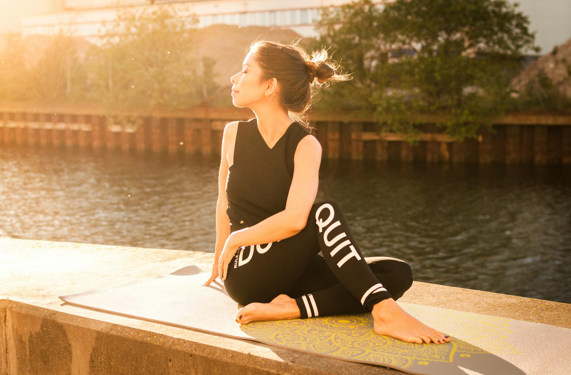 woman wearing black fitness outfit performs yoga near body of water