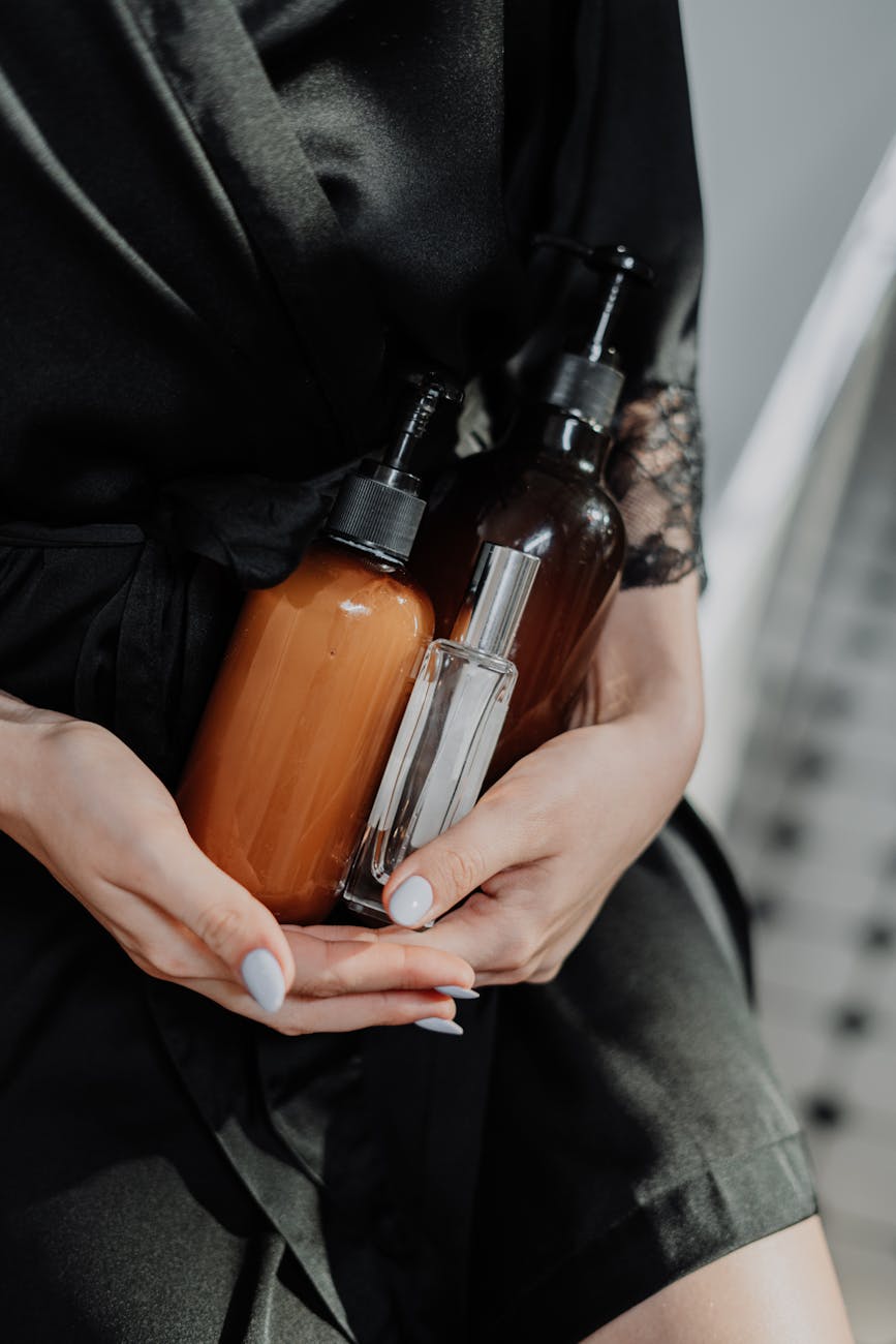 person in black silk robe holding glass pump bottles