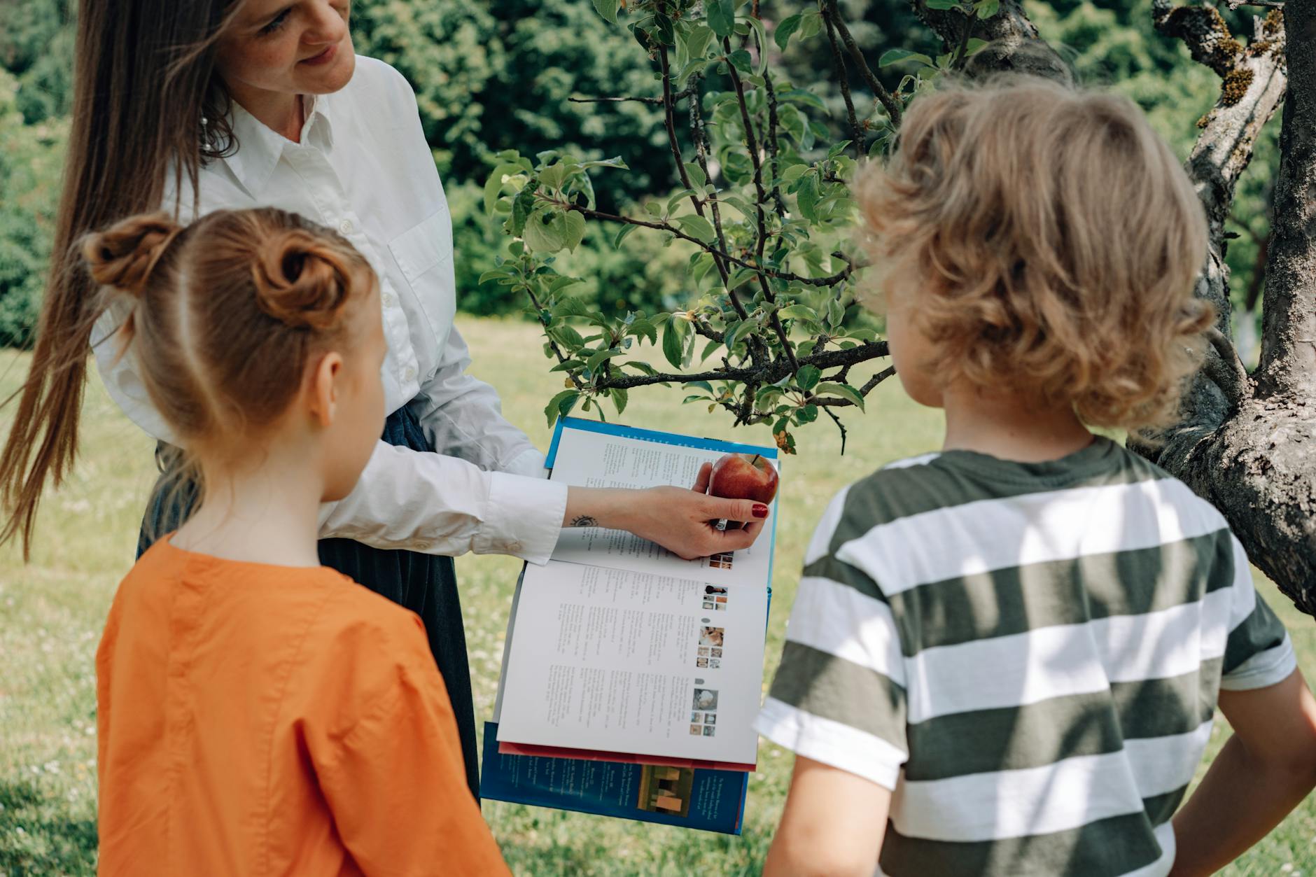 a woman holding an apple and a book in front of the kids