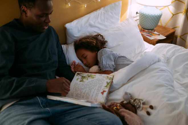 father reading bedtime story for his daughter while lying down on the bed