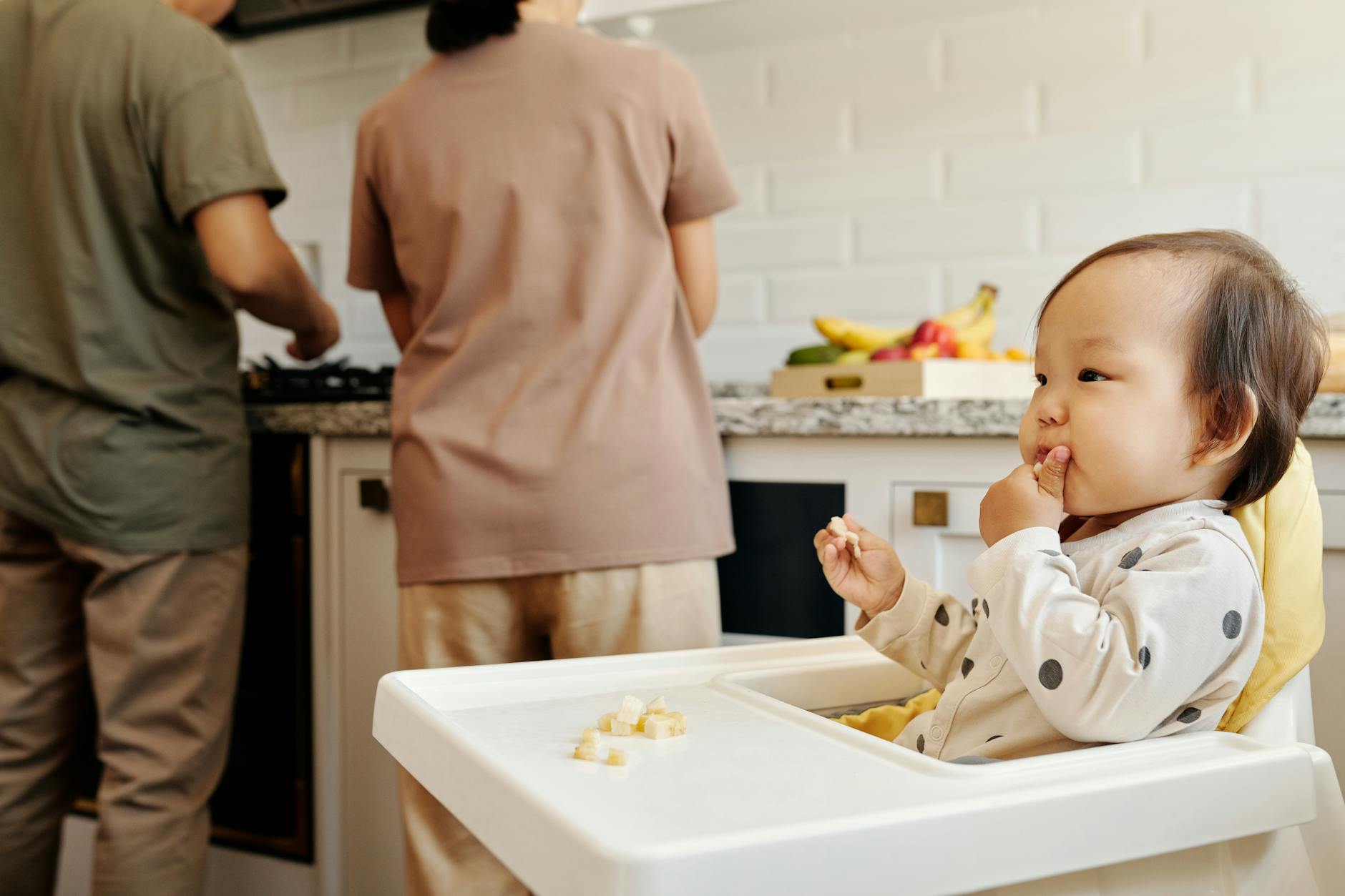 a toddler in polka dots baby clothes sitting on high chair