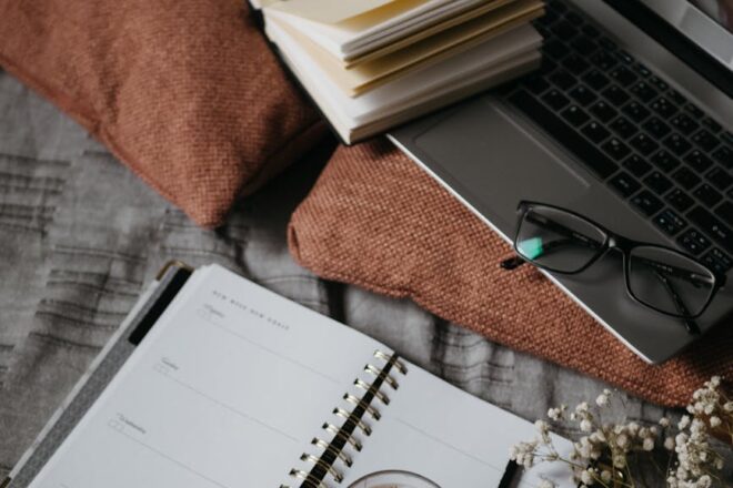 black and silver laptop computer beside white notebook and black framed eyeglasses