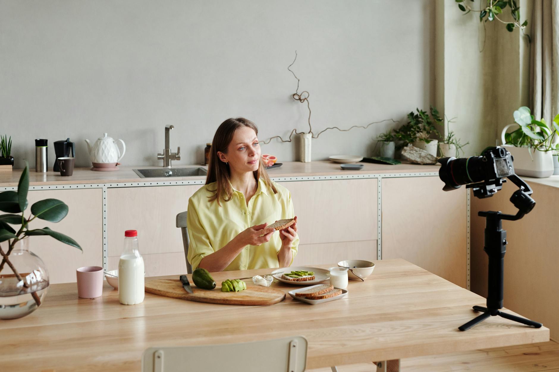 woman in yellow long sleeves filming herself while making an avocado toast